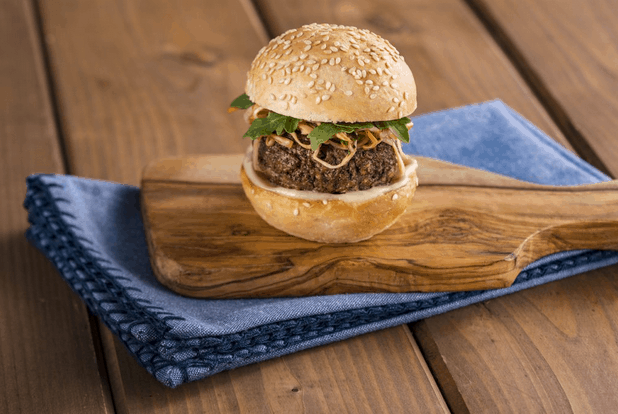 An Impossible Burger Slider from Disney, served on a wooden board with a blue napkin, finished with fresh greens and crispy onions—perfect for park-goers looking for a gourmet plant-based bite.