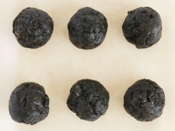 Six round, dark chocolate cookie dough balls arranged in two rows on a light background, ready to become magical Mickey Pumpkin Truffles—a sweet Halloween treat inspired by Disney Parks festivities.