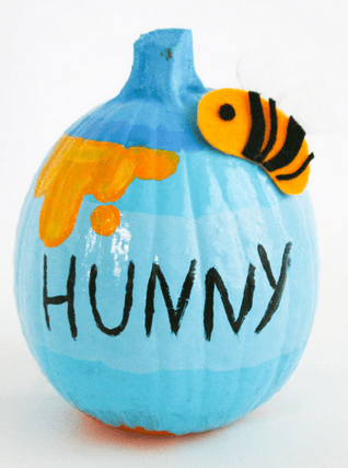 A Winnie the Pooh-inspired blue pumpkin at Disney Parks, featuring "HUNNY" lettering, drips of yellow honey, and a felt bee—an enchanting addition to your next Hunny Pot Pumpkin craft or Halloween celebration.