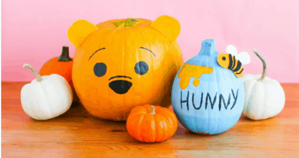 Winnie the Pooh and his iconic "Hunny Pot" come to life on these delightfully themed pumpkins, channeling all the charm of a fall celebration at a Disney park, with smaller decorative pumpkins accenting the festive scene.