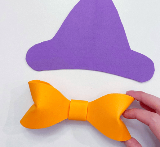 A guest displays a bright yellow bow beside a flat purple Minnie Witch hat, perfect for Disney Halloween festivities, on a crisp white surface.
