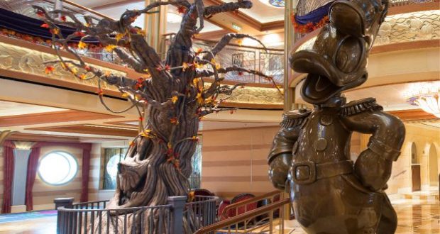 Donald Duck statue alongside a playful autumn Pumpkin Tree inspired by Disney Cruise Line, showcased within the lavish, storybook-style interior of a Disney park attraction.