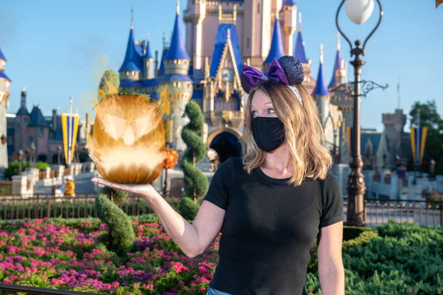 A guest at Disneyland stands in front of Sleeping Beauty Castle, sporting iconic Mickey ears and a face mask, holding a glowing magical orb—an enchanting PhotoPass moment to remember forever.