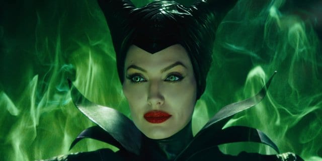 Maleficent, in her iconic horned headdress and dark costume, stands before swirling green flames with a commanding presence—capturing the dramatic magic fans love in Disney’s unforgettable Halloween celebrations.