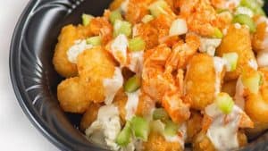 Savor crispy tater tots loaded with buffalo chicken, blue cheese chunks, fresh celery, and a drizzle of ranch dressing, all served on a sleek black plate—the fan-favorite snack that's making its much-anticipated return as Friar’s Nook reopens at Magic Kingdom.