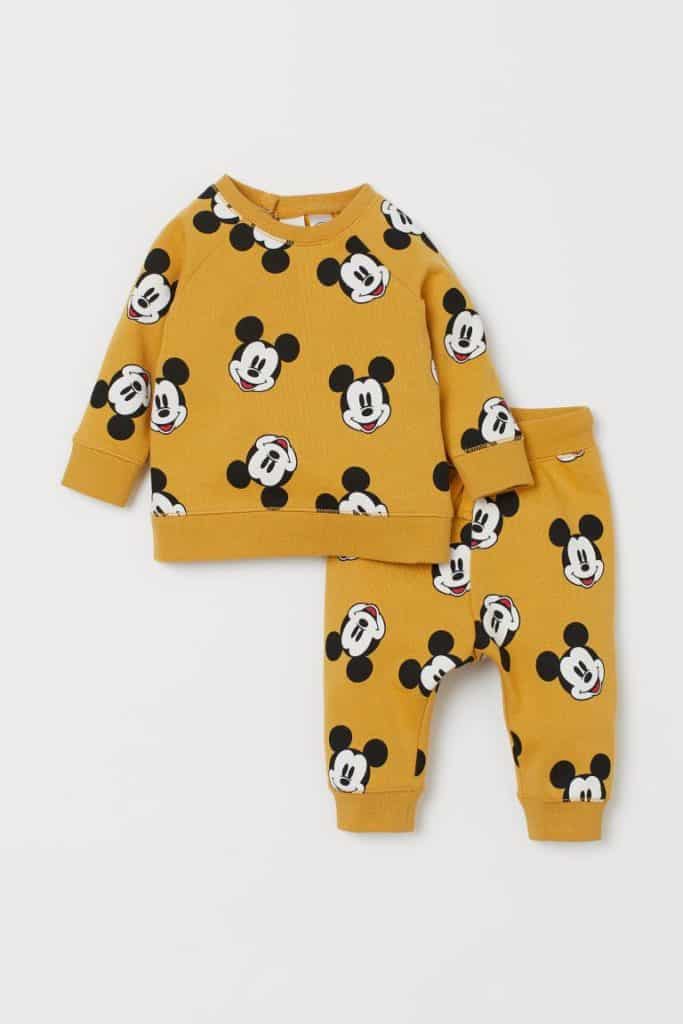 This sunny yellow toddler outfit, inspired by the magic of Disney parks, showcases long sleeves and pants playfully adorned with iconic Mickey Mouse faces for a whimsical touch. A perfect choice for little fans dreaming of their next visit to Disney World or exploring the latest H&M x Disney collection!.