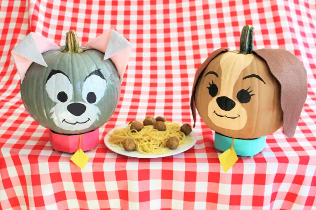 At a Disney-inspired display, two no-carve pumpkins decorated as beloved cartoon dogs create a magical scene as they sit at a table with a shared plate of spaghetti and meatballs, capturing the whimsical spirit of Halloween at the parks.