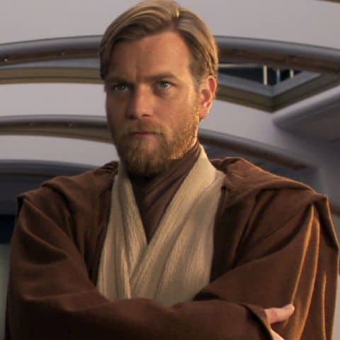 Obi-Wan Kenobi, dressed in signature Jedi robes with arms crossed and a serious expression, poses indoors as seen in the Disney+ series.
