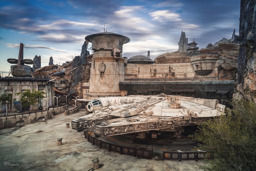 The Millennium Falcon docked in Star Wars: Galaxy’s Edge, surrounded by towering rocky spires and high-tech outposts, awaiting Disney PhotoPass photographers to help guests capture their epic adventure.
