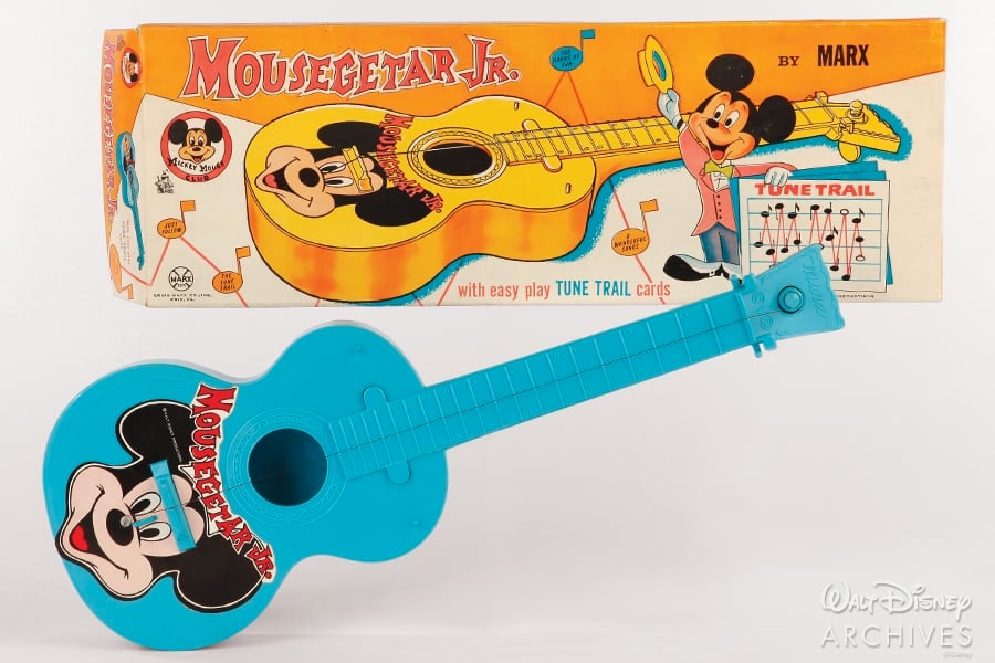 A bright blue toy guitar featuring Mickey Mouse in honor of 65 Years of Disney magic, displayed beside its vibrant retro box marked "Mousegetar Jr. by Marx," perfect for any Disney Parks collector or fan of classic Magic Kingdom memorabilia.