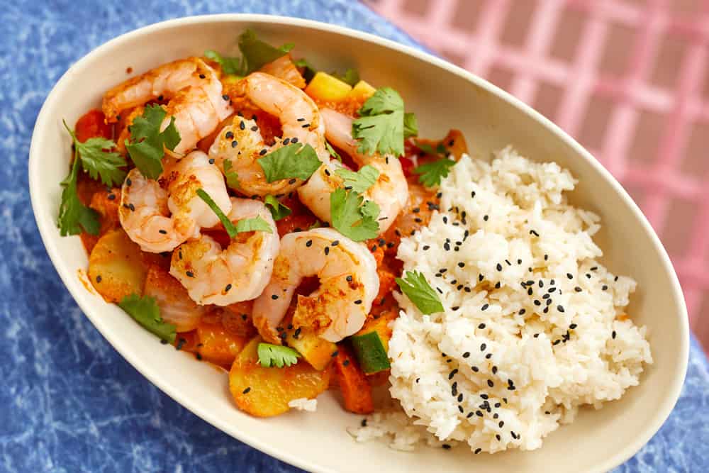 A delicious new dish at Disney's Hollywood Studios features succulent shrimp sautéed with vegetables and fresh cilantro, served alongside fluffy white rice sprinkled with black sesame seeds on an oval plate. This exciting addition to the park’s menu is ideal for guests craving bold, fresh flavors during their magical culinary adventure.