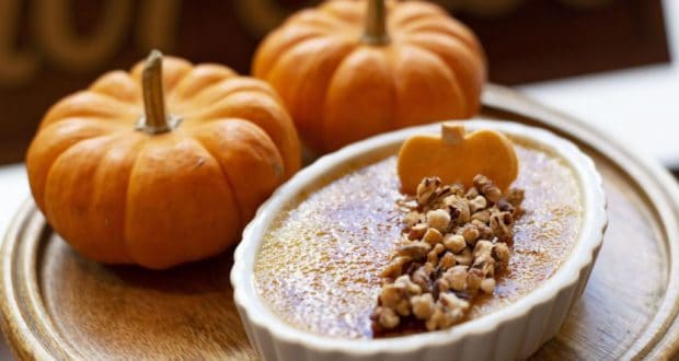 Get into the festive spirit at the park with a special pumpkin creme brulee, topped with pecans and surrounded by two mini pumpkins on a rustic wooden tray—an autumn-inspired treat sure to delight fans looking for seasonal flavors between rides and shows!.