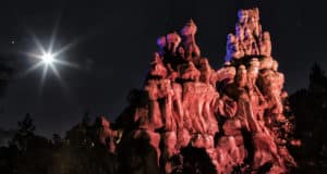 Iconic rock formation illuminated by dramatic red and blue lighting beneath a dazzling moon and sparkling stars, evoking the enchanting, otherworldly atmosphere of Disney’s nighttime spectaculars and magical moonlit moments in the parks.