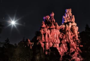 Iconic rock formation illuminated by dramatic red and blue lighting beneath a dazzling moon and sparkling stars, evoking the enchanting, otherworldly atmosphere of Disney’s nighttime spectaculars and magical moonlit moments in the parks.