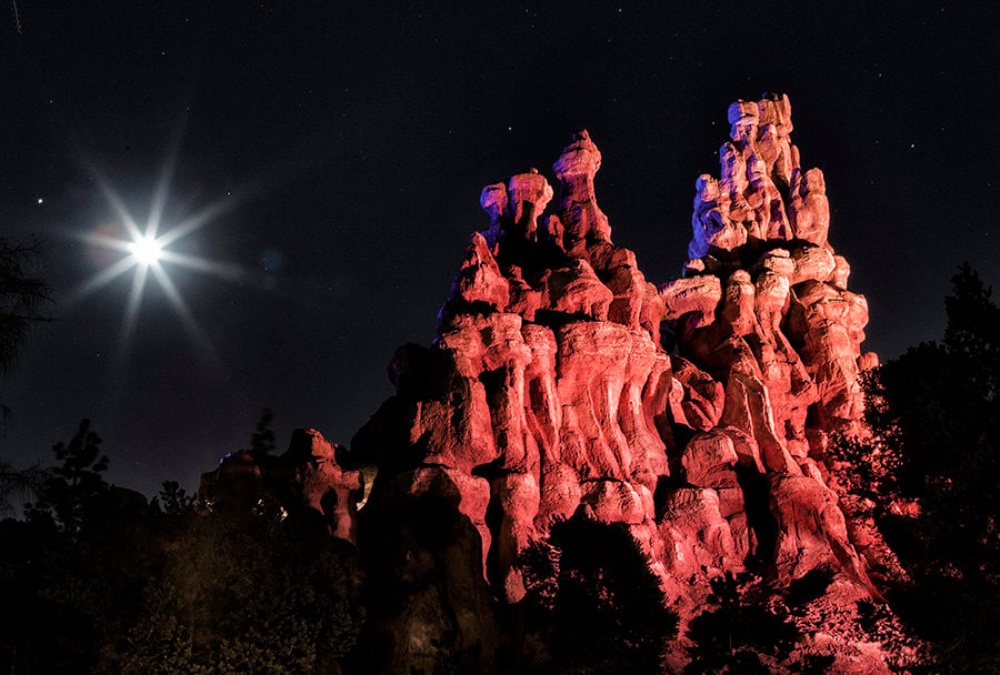 Iconic rock formation illuminated by dramatic red and blue lighting beneath a dazzling moon and sparkling stars, evoking the enchanting, otherworldly atmosphere of Disney’s nighttime spectaculars and magical moonlit moments in the parks.