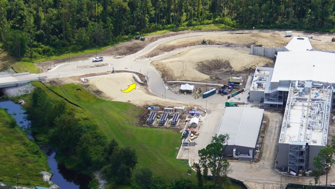 Aerial view of construction progress on the Star Wars: Galactic Starcruiser at Walt Disney World, with busy work zones, new structures rising, equipment in action, and a yellow arrow pointing the way along a dirt road—capturing excitement as this immersive resort expansion takes shape.
