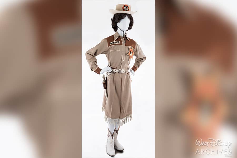 A headless display dressed in a classic beige cowgirl outfit—complete with hat, sheriff badge, and white boots—strikes a hands-on-hips pose reminiscent of the iconic Mouseketeers’ western look from The Mickey Mouse Club’s earliest days during Disney’s golden era.