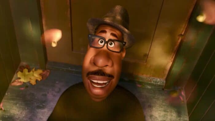 Joe Gardner from Disney and Pixar’s "Soul" gazes upward, wearing his signature glasses and hat, as autumn leaves drift down around him on a wooden porch—a heartfelt scene capturing the magic fans love about Disney+ animated hits.