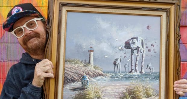 A guest sporting glasses displays a framed artwork that cleverly fuses iconic Star Wars characters with a nostalgic coastal lighthouse scene, reminiscent of classic thrift shop art—perfect for fans who love immersive worlds and imaginative nostalgia.