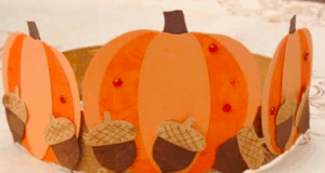 A festive paper crown inspired by fall festivities at the park, adorned with playful orange pumpkins, brown acorns, and cheerful red dots—an enchanting accessory for young guests during Thanksgiving-themed events, displayed on a bright surface.