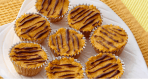 Eight allergy-friendly pumpkin muffins topped with chocolate drizzle, inspired by seasonal theme park treats, are artfully displayed on a white plate over cheerful yellow fabric—ready to delight fans of festive park snacks.