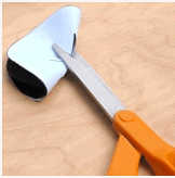 Scissors with orange handles cutting a piece of white paper on a wooden table, perfect for crafting magical Thanksgiving decorations inspired by Disney parks.