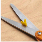 A pair of open scissors with a small yellow plastic piece between the blades rests on a wooden surface, ready for fans to create magical Disney Thanksgiving crafts like Butternut Pluto—ideal for adding a touch of festive cheer to your next trip to Walt Disney World or Disneyland’s seasonal celebrations.