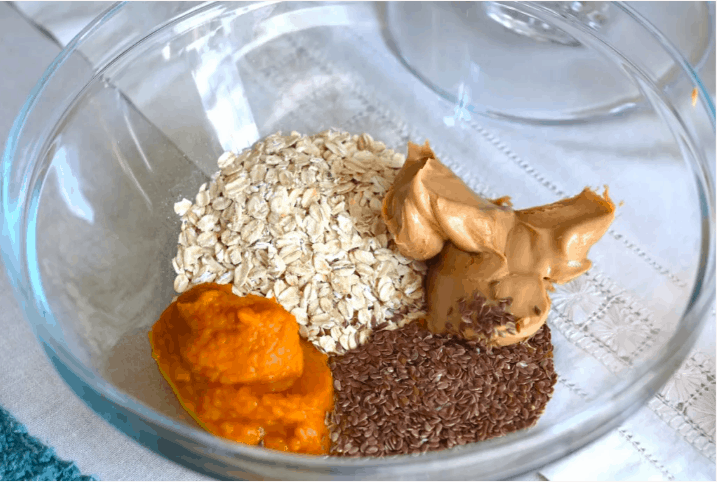 A glass bowl filled with oats, peanut butter, flax seeds, and pumpkin puree sits on a crisp white cloth—magical ingredients ready to whip up Pumpkin Energy Balls that would keep any theme park adventurer fueled for a day of thrills and fall festivities.