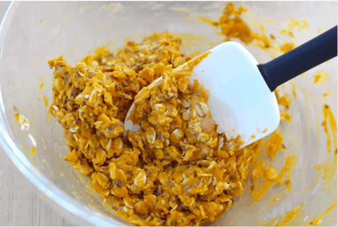 A spatula swirls oats and pumpkin batter in a glass bowl, whipping up Pumpkin Energy Balls inspired by those magical fall treats you’d find along Main Street at a theme park.