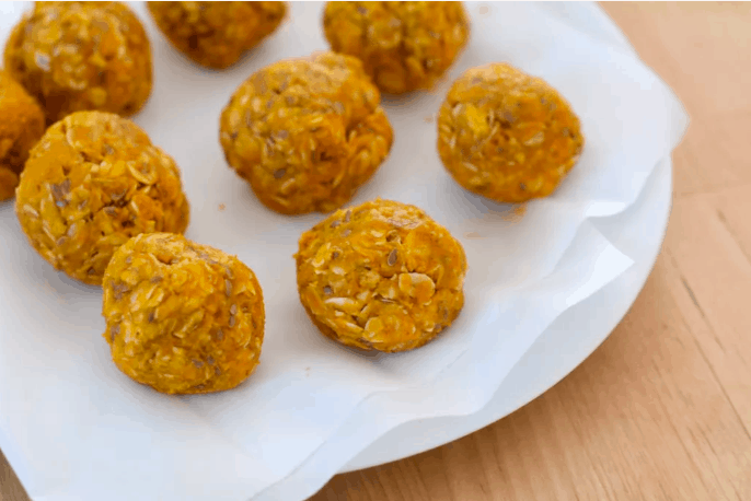 Pumpkin Energy Balls and oat snack balls arranged on a white plate with parchment paper, set atop a light wooden table—these festive bites are ready to fuel your day at Disney World or keep you energized between rides at Universal Studios, bringing theme park magic to your fall snacking.
