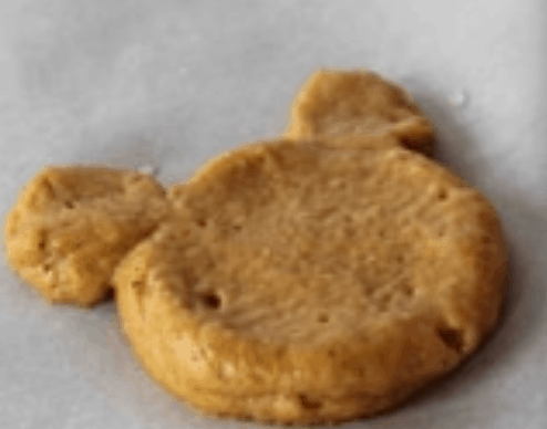 A delightful Mickey Mouse-shaped cookie sits atop parchment paper, capturing the festive magic of Disney park treats like the iconic Mickey Pumpkin desserts and playful Whoopie Pies served throughout the parks.