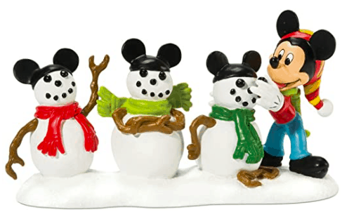 Mickey Mouse, sporting his signature hat, greets guests beside three snowmen dressed in Mickey ears and vibrant scarves atop sparkling snow. The charming scene adds festive magic to the heart of the Mickey Christmas Village at Disney Parks.