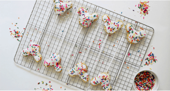 Whimsical animal-shaped cookies decorated with white icing and rainbow sprinkles rest on a cooling rack, echoing the playful spirit of theme park treats. Sprinkles scattered around evoke the festive atmosphere of a day at your favorite entertainment destination—perfect for making celebrations magical and sharing smiles like souvenirs from a memorable adventure.