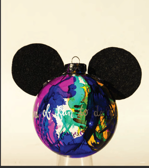 A vibrant Mickey-inspired glass ornament with signature black ears, displayed on a clear pedestal against a simple backdrop—ideal as a magical keepsake or DIY craft for Disney fans and theme park enthusiasts.