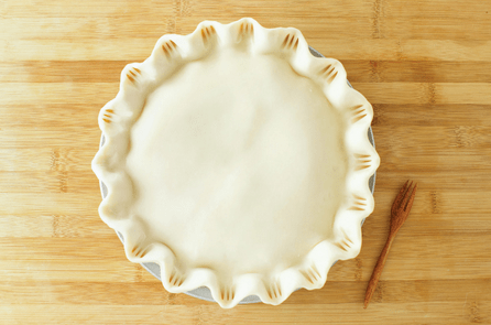 An unbaked pie with crimped edges rests in a dish on a wooden surface, a small fork beside it—capturing the homey vibe of delicious desserts you’d find at Disney’s Animal Kingdom, just steps away from the legendary Tree of Life.