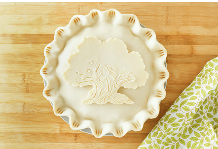 Unbaked pie featuring a dough design inspired by the Tree of Life at Disney’s Animal Kingdom, set on a wooden table alongside a napkin with leafy Disney-style patterns.