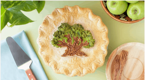 A whimsical pie featuring a Tree of Life crust inspired by Disney’s Animal Kingdom, displayed beside green apples and classic pie-cutting utensils for a magical at-home park experience.