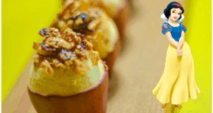 Baked apples with crumble topping on a cheerful yellow surface, inspired by the Snow White storybook recipe, with Snow White herself greeting guests beside the treats in a magical theme park setting.