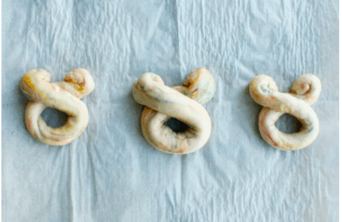 Three golden, Mickey-shaped pretzel twists evoke the magic of Disney parks, playfully arranged like classic Disney bears on a bright, whimsical backdrop for a treat straight out of your favorite theme park snack stand.