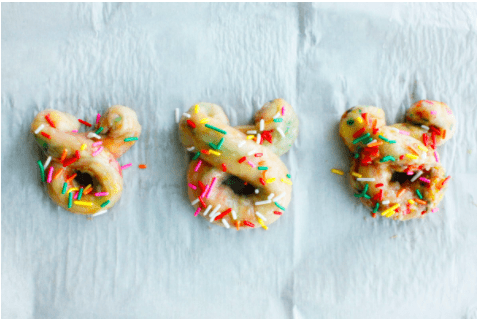 Bear-shaped donuts topped with vibrant sprinkles rest on parchment paper, evoking the whimsical charm of Disney park treats and capturing the nostalgia of fresh-baked goodies from Main Street USA.