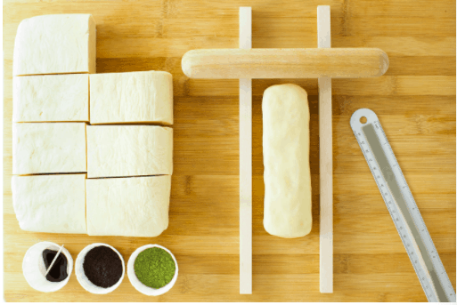 Rectangular dough pieces, a dough cutter, a ruler, and three small bowls on a wooden surface—ready for baking Colorful Cookies inspired by your favorite Mickey and Friends treats from Disney Parks or iconic Icebox Cookies seen in classic Disney celebrations.