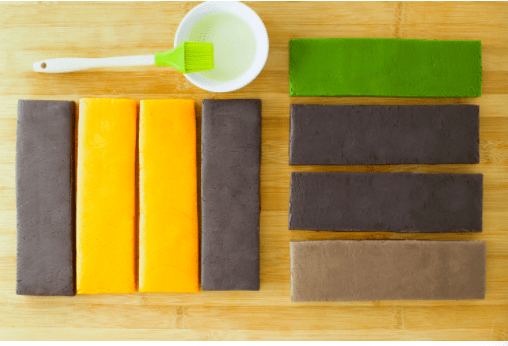 Vibrant pastry sheets in orange, green, brown, and gray rest next to a brush and small bowl on a wooden counter, ready for guests to craft their own magical icebox cookies at Main Street Confectionery in Disneyland.