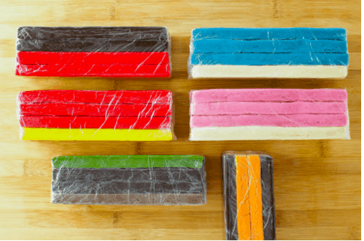 Six stacks of colorful, layered icebox cookies inspired by Mickey and Friends, individually wrapped in plastic and displayed on a wooden table, evoking the fun and playful spirit found at Disney Parks.