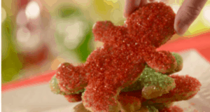 A guest selects a festive red-sugar coated Disney Gingerbread Cookie from a plate of holiday treats, evoking the enchantment and nostalgia of holiday celebrations at Disney parks.