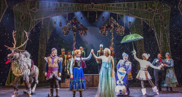 Elsa, Anna, and other Frozen characters light up the stage in vibrant costumes during a snowy musical number, using dazzling props and lively expressions to immerse Disney Cruise Line fans in the magic of an enchanting virtual Frozen Musical experience.