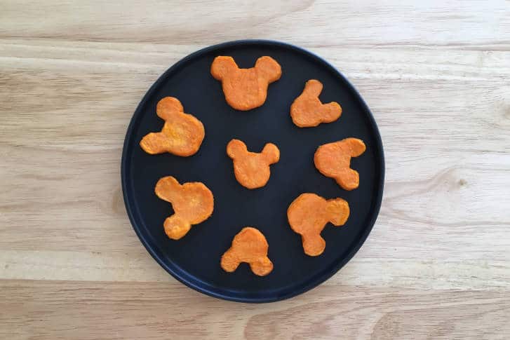 Celebrate Thanksgiving Disney style with eight Mickey-shaped sweet potato nuggets, perfectly arranged in a circle on a sleek black plate set atop rustic wood—bringing a touch of magic to your holiday feast.