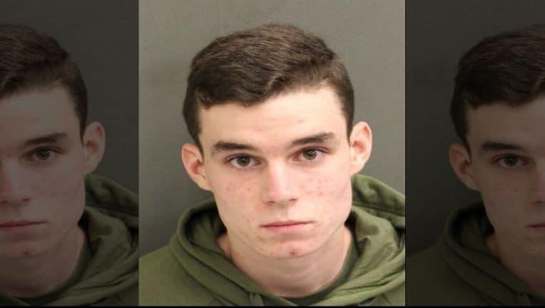 A young man with short brown hair in a green hoodie stares directly at the camera, set against a dark backdrop. His appearance calls to mind the individual reportedly seen at Disney Springs impersonating security staff while carrying a BB gun.