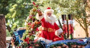 Santa Claus greets guests from a dazzling holiday float adorned with sparkling Christmas ornaments and lush greenery, spreading festive cheer throughout EPCOT at Walt Disney World.