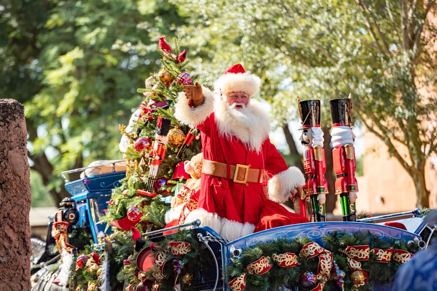 Santa Claus greets guests from a dazzling holiday float adorned with sparkling Christmas ornaments and lush greenery, spreading festive cheer throughout EPCOT at Walt Disney World.