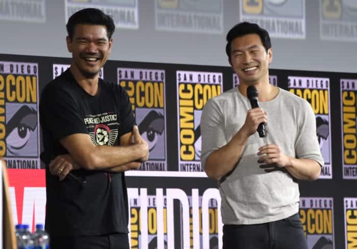Two Disney representatives sharing a lively conversation onstage at San Diego Comic-Con, surrounded by iconic Comic-Con banners, as they reveal exciting upcoming movies and future attractions eagerly awaited by Disney fans and theme park enthusiasts.